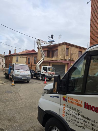Vehículos de trabajo en una calle, con una grúa cerca de un edificio de dos plantas.